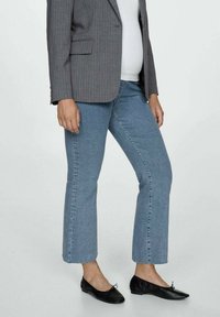 Jeans cropped de mezclilla azul claro con pierna recta, combinados con una chaqueta gris de rayas y zapatos planos negros. La tela parece tener una textura ligera.