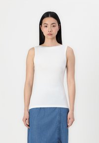 Weißes ärmelloses Top aus glattem Stoff mit rundem Halsausschnitt, kombiniert mit einem blauen Jeansrock mit seitlichen Stichdetails.