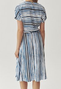 Abito a righe con una combinazione di colori blu, bianco e nero. Maniche corte, lunghezza al ginocchio e una gonna fluida con una vita legata.