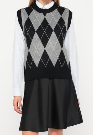 Kvinde iført sort og grå argyle-strikket vest over hvid skjorte med knapper og sort A-formet nederdel, vist fra nakke til midt på låret.