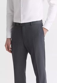 Ciemnoszare spodnie garniturowe z delikatnym wzorem w prążki, dopasowany krój, gładki materiał i szlufki na pasek; noszone z białą koszulą z guzikami.
