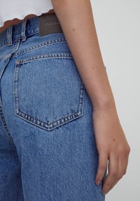 Jean en denim bleu clair avec un design à cinq poches, des coutures visibles et une étiquette de ceinture texturée avec "PULL&BEAR" embossée.