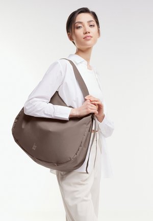 Sac à bandoulière marron rembourré avec un design incurvé et une fermeture à cordon. Matériau doux, comportant un logo sur le devant.