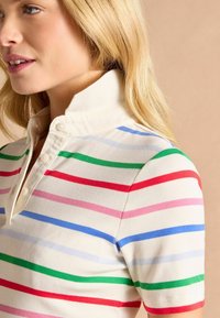 Gestreiftes Poloshirt mit Kragen, das horizontale Linien in Rot, Grün, Pink und Blau auf einem cremefarbenen Hintergrund zeigt. Texturiertes Rippmaterial.