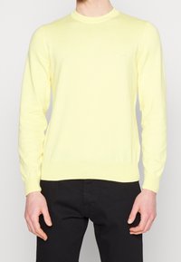Helle gelbe Strickpullover mit rundem Ausschnitt und langen Ärmeln. Mit gerippten Bündchen und Saum. Logo dezent auf der Brust platziert.
