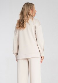 Jasnobeżowy zestaw odzieży domowej składający się z luźnego swetra z opadającymi ramionami i pasujących szerokich spodni. Miękka, teksturowana tkanina.