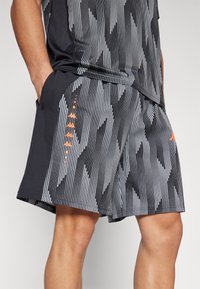 Zwart-witte sportshorts met een patroon van verticale lijnen, oranje logo-accenten en zakken; gemaakt van lichtgewicht, ademend materiaal.