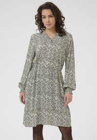 Rochie cu mânecă lungă și decolteu în v, cu un model în valuri alb-negru, talie strânsă și mansete cu volane.