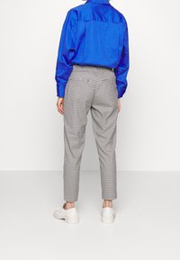 Chemise en satin bleu à manches longues ; pantalon à carreaux taille haute ; baskets blanches à semelles épaisses. Coupe ajustée et motif à carreaux subtil.