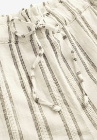 Gros plan sur un tissu en lin blanc avec des rayures noires verticales et un cordon noué à la ceinture élastique d’un vêtement.