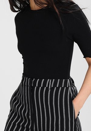 Schwarzes, geripptes Kurzarmoberteil, kombiniert mit hoch taillierten schwarz-weißen gestreiften Hosen, die eine maßgeschneiderte Passform und Seitentaschen aufweisen.