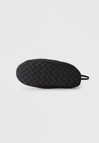Chaussure noire rembourrée avec une semelle texturée, présentant un motif répétitif de petites formes ovales. Inclut une petite boucle pour une manipulation facile.