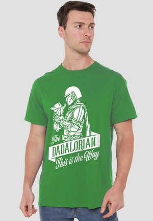 Man wearing green t-shirt showing white illustration of Mandalorian holding baby Yoda with text "The Dadalorian This is the Way."
