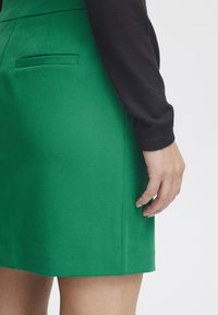 Grön skräddarsydd kjol med en mjuk textur, sidoficka och en lätt A-linjeform, tillsammans med en svart långärmad topp.