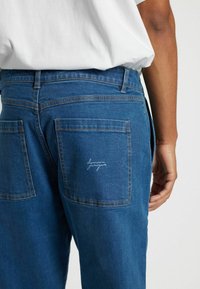 Modre jeans hlače iz denima s ravnim krojem, dvema zadnjima žepoma in diskretnim vezenim detajlom na desnem žepu.
