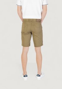 Pantaloni corti color khaki con taglio dritto, due tasche posteriori e dettagli cuciti, abbinati a scarpe bianche con accenti blu navy.