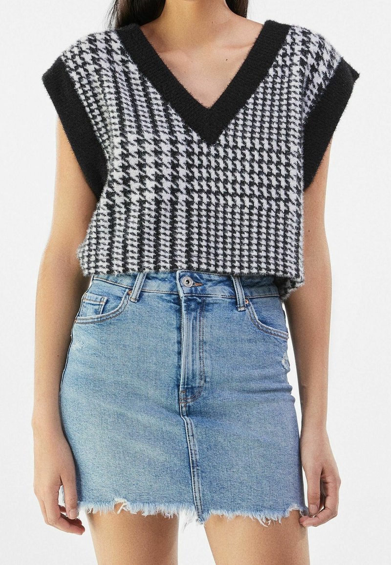 Černobílý houndstooth cropped svetr s výstřihem do V, spárovaný se světle modrou džínovou mini sukní s třepeným lemem.