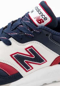 Baskets New Balance en bleu marine, blanc et rouge. Composées de suède texturé et de cuir lisse, avec un logo brodé et des lacets contrastants.