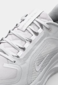 White athletic shoe featuring a mesh body, textured accents, flat laces, padded collar, and a prominent Nike Swoosh logo in a tonal design.
