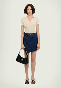 Μπεζ μπλουζάκι κοντό μανίκι, ναυτικό μπλε μίνι φούστα από τζην, μαύρη τσάντα ώμου και μαύρες σανδάλες με λουριά. Λείες υφές; μινιμαλιστικός σχεδιασμός.