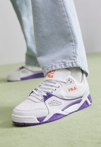 Vita sneakers med lila accenter, med en strukturerad design, snörning och logodetaljer. Bärs med ljusblå denim.