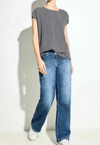 Top corto a maniche corte con fantasia in bianco e nero abbinato a jeans blu larghi, con aperture laterali, e sneakers bianche.