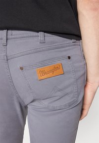 Grijze Wrangler jeans met een leren patch op de achterzak, contrasterende stiknaad en een slim-fit ontwerp.