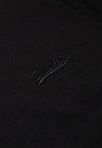 Sort stof med en blød tekstur, der har et præg af "SuperDry" logo i matchende sort. Enkel og ren design uden yderligere accenter.