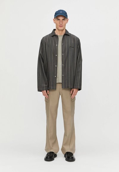 Chemise à rayures dans des couleurs sombres, associée à un t-shirt gris et un pantalon cargo beige. Matériau texturé, coupe décontractée, chaussures noires.