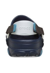 Marineblauwe Crocs-sandalen met verstelbare bruine riem, witte accenten bij de hak, textuur rubberen loopzool en geperforeerd ontwerp voor ademend vermogen.