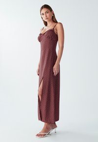 Dlhé bordové šaty s bielymi bodkami, nastaviteľné ramienka, bočný rozparok a volánkový detail v mäkkej látke.