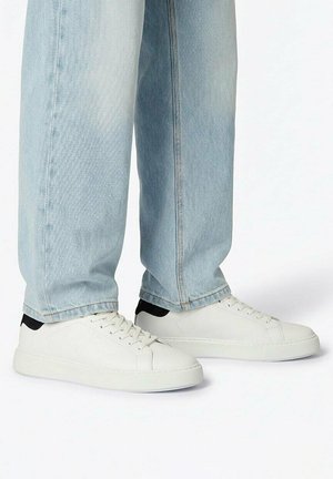 Weiße Low-Top-Sneaker mit schwarzen Fersenlaschen, getragen zu hellblauen Jeans mit weiter Beinweite.