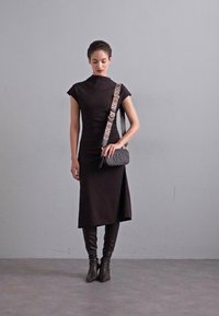 Black fitted dress with short sleeves, asymmetrical hem, paired with knee-high brown leather boots and a small crossbody bag with patterned strap.