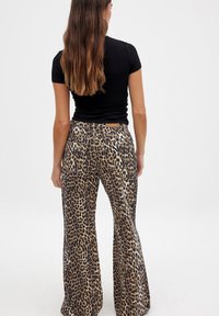 Pantalones acampanados de estampado de leopardo en tonos marrón y negro, con cintura alta, piernas anchas y dos bolsillos traseros. Textura de tela suave.