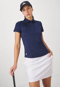 Polo shirt marine avec une patte de boutonnage à trois boutons et un détail de logo. Associé à une jupe blanche, texture lisse, coupe sportive et manches courtes.