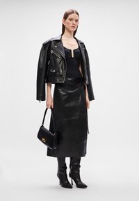 Musta nahkamoottoripyörätakki hopeisilla yksityiskohdilla, tiukka musta bodysuit, pitkä nahkahame, polvipituiset korkokengät ja pieni musta käsilaukku.