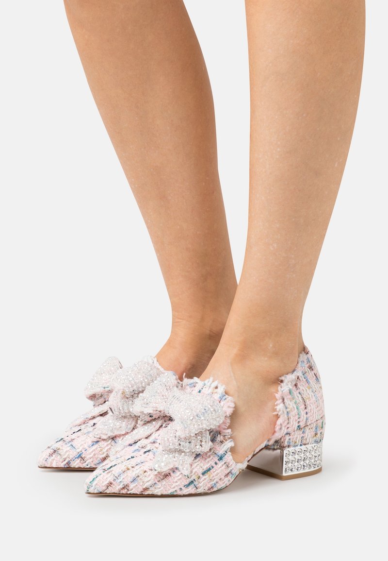 Chaussures à bout pointu avec talons bas en tissu tweed multicolore, grands nœuds texturés et strass sur les talons blocs, portées pieds nus.