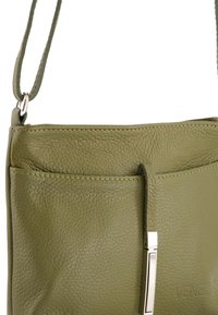 Grüne Leder-Crossbody-Tasche mit strukturiertem Finish, einem verstellbaren Tragegurt und einem metallischen Akzent auf der Fronttasche.