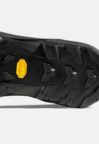 Zwarte rubberen schoenzool met diepe groeven en een geel Vibram-logo in het midden voor verbeterde grip en duurzaamheid.