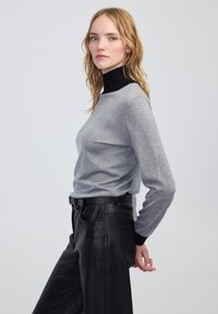 Pull gris à manches longues avec un col roulé noir, associé à un pantalon en cuir noir. Texture lisse, coupe décontractée et design simple.