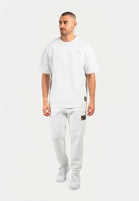 Wit T-shirt met korte mouwen en bijpassende sweatpants van een zachte, gladde stof. Opvallende zwart-rode logopatch op de broek.