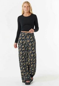 Zwarte crop top met lange mouwen gecombineerd met wijde, bloemenprint broek met blauwe en gele bloemen op een donkere achtergrond. Zwarte platform sandalen.