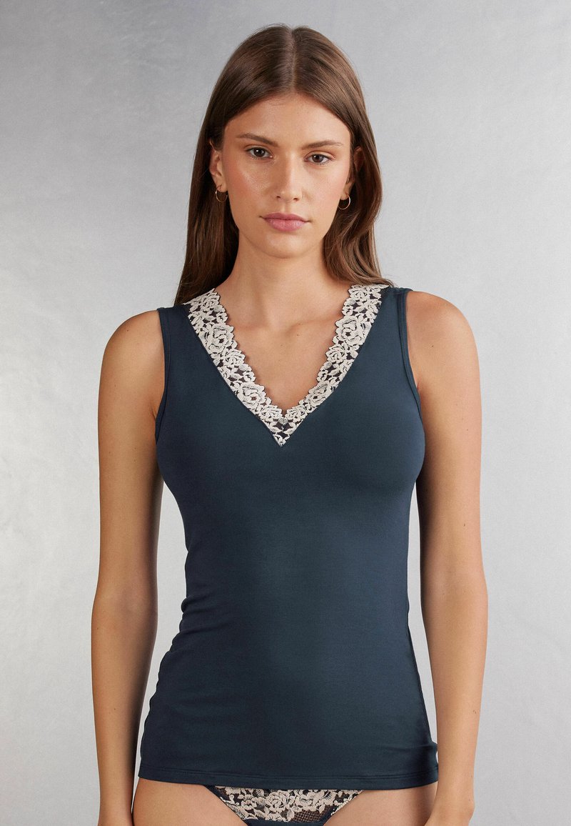 Námořnická modrá tílko s výstřihem do V, zdobené bílou krajkou. Přiléhavý střih s hladkým materiálem, ukazuje elegantní siluetu.