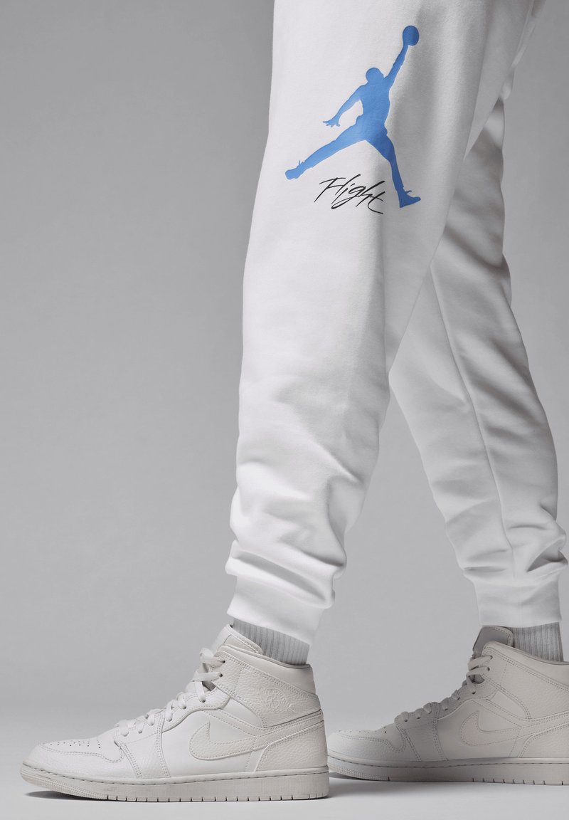Weiße Jogginghosen mit blauem Jumpman-Logo und "Flight"-Schriftzug verfügen über gerippte Bündchen. Kombiniert mit weißen High-Top-Sneakern mit strukturierten Akzenten.