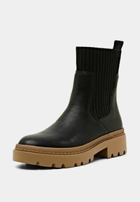 Bottines noires en cuir avec tige en tissu côtelé, semelle épaisse beige, et une languette à l'arrière pour un enfilage facile. Accents texturés sur les côtés.