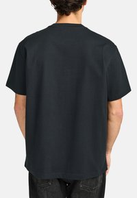 Camiseta de algodón negra con un corte relajado, mangas cortas y cuello redondo; diseño minimalista y textura suave.