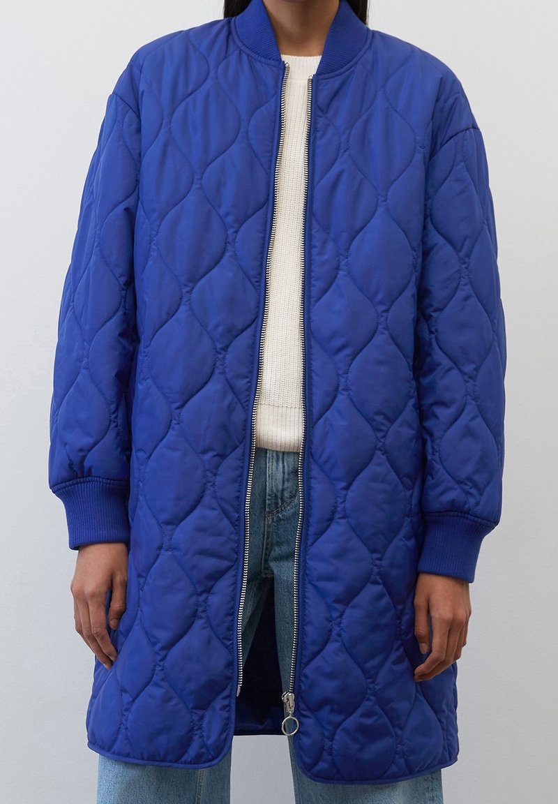 Veste bomber bleue matelassée avec poignets et col côtelés, dotée d'une fermeture éclair argentée et d'un design texturé et rembourré.