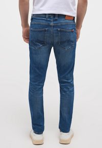 Modré džíny z denimu se středním střihem, obsahující dvě zadní kapsy, hnědou koženou nášivku a detaily prošívání na kapsách.