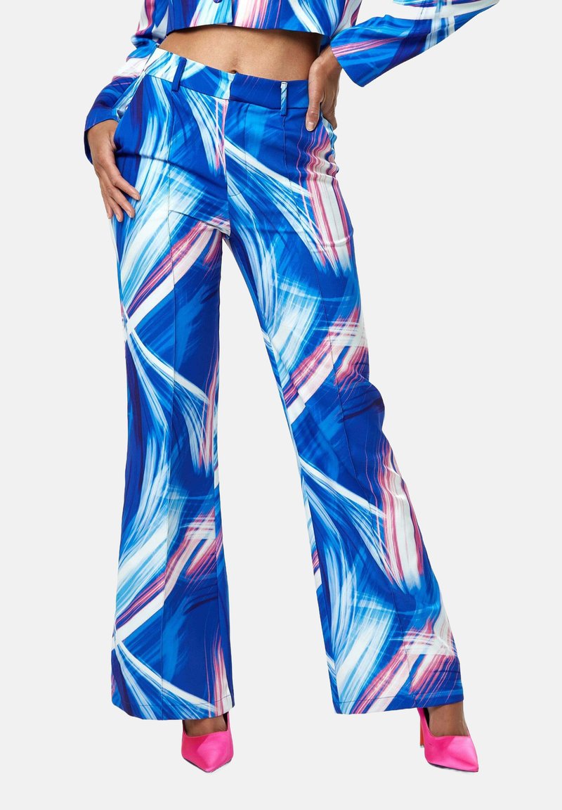 Blue patterned flared pants with white and pink abstract strokes, featuring a smooth texture and flat front pockets. Worn with pink pointed heels.
