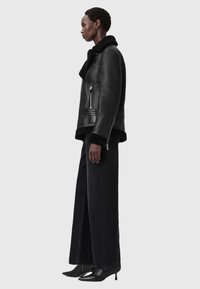 Czarna skórzana kurtka z futrzanym kołnierzem, bocznymi kieszeniami na zamek i krojem na krótką długość. W zestawie z czarnymi, szerokimi spodniami z wysokim stanem i obcasami.